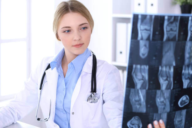 Doctor woman examining x-ray picture near window in hospital. Surgeon or orthopedist at work. Medicine and healthcare concept. Blue colored blouse of a therapist looks good.