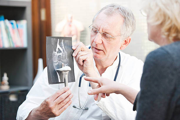 A mature medicine presenting a total knee arthroplasty and x-ray to a female patient. This is a so called duohead prosthesis.
