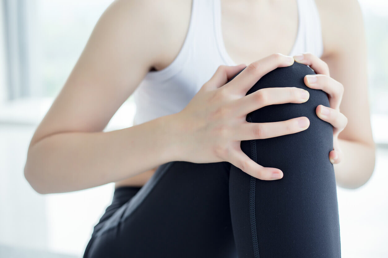 Slim woman sitting on floor touching her injured knee.