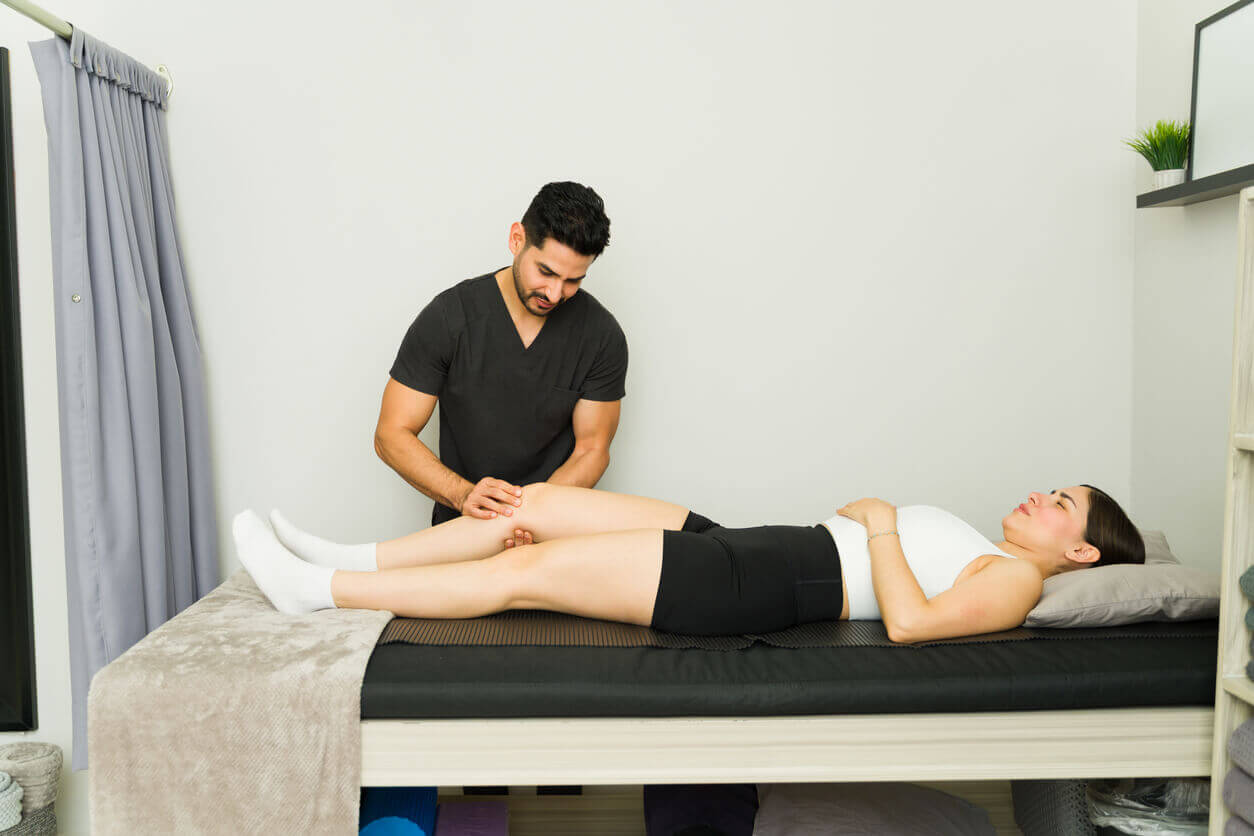 A sports medicine doctor is performing a targeted knee massage to help a female patient recover in a modern rehabilitation setting.