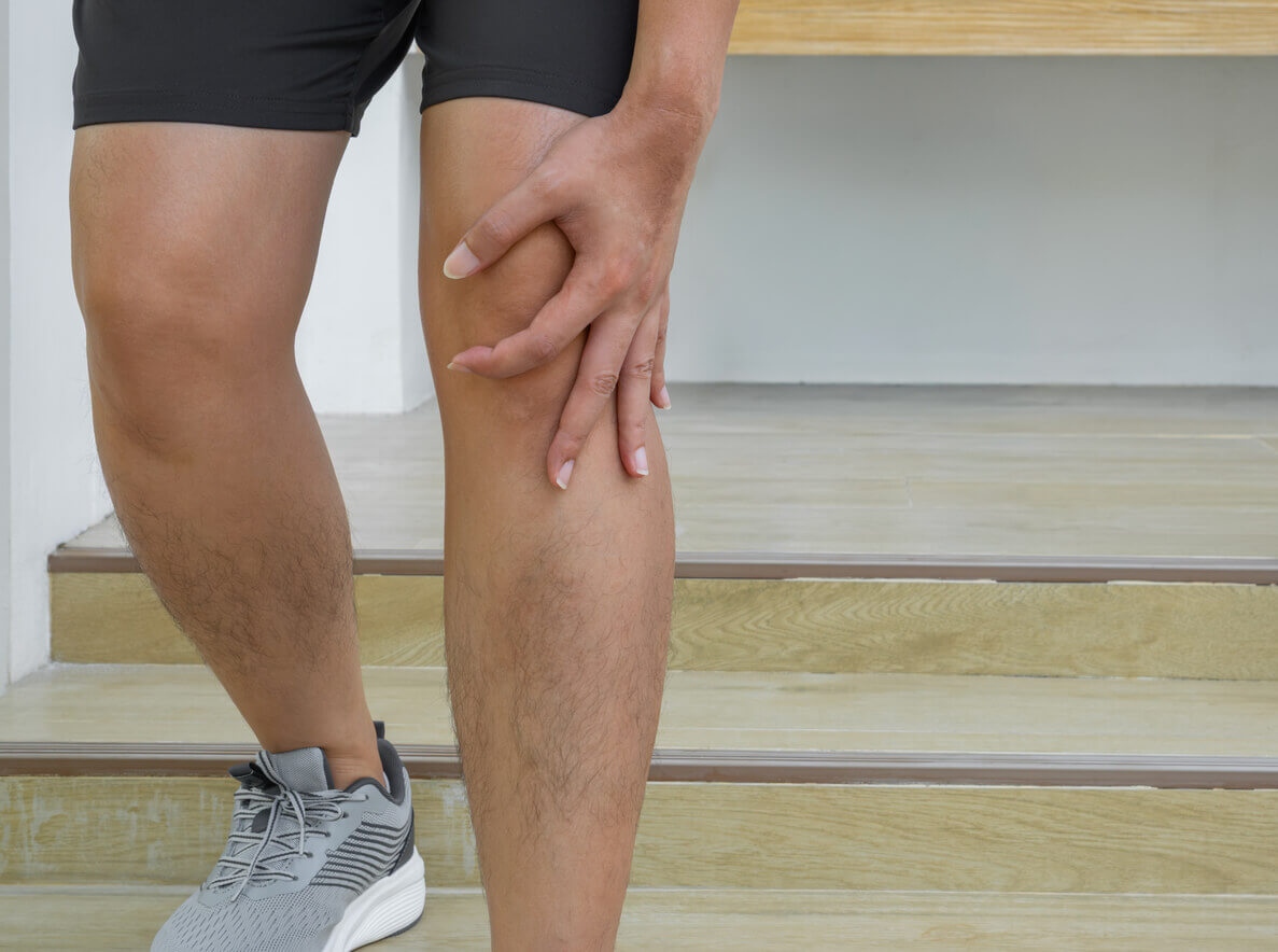 A man on shorts experiences knee pain while descending stairs post-running.