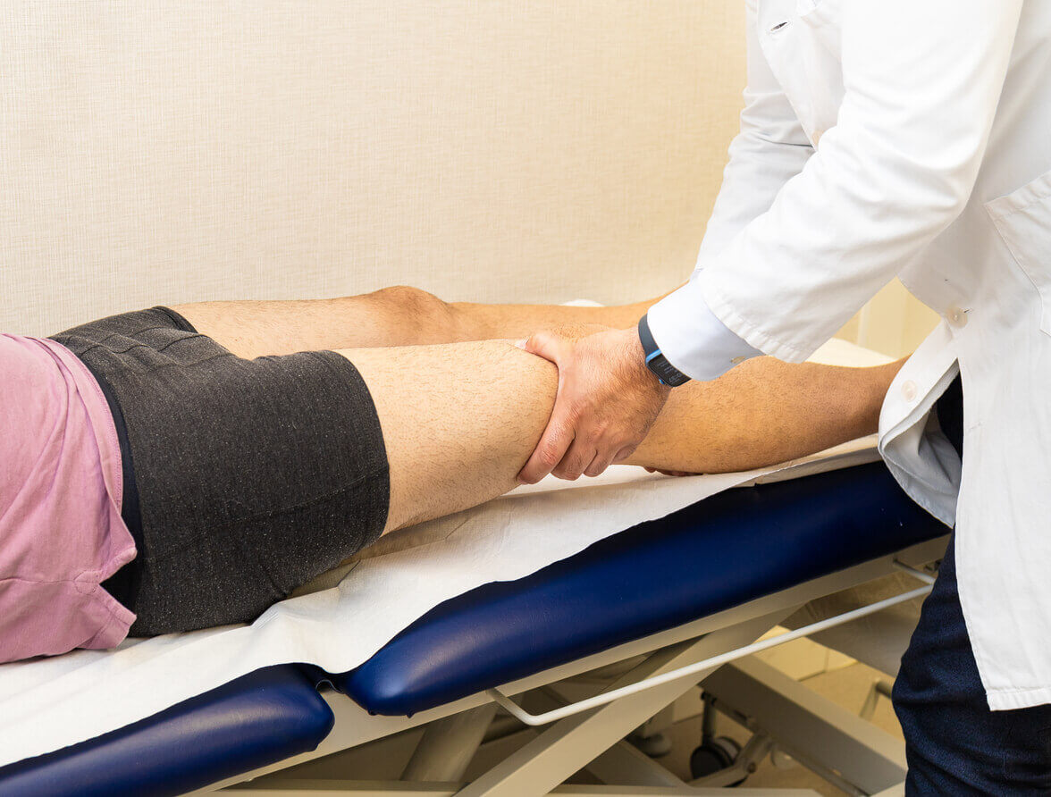 Orthopedic surgeon during consultation is examining patient’s knee